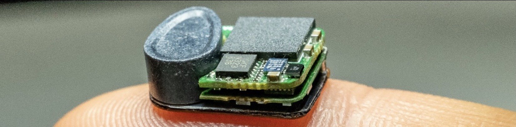 The lab's newest implantable device for mice, two stacked circuit boards beside a cylindrical component, resting on a fingertip